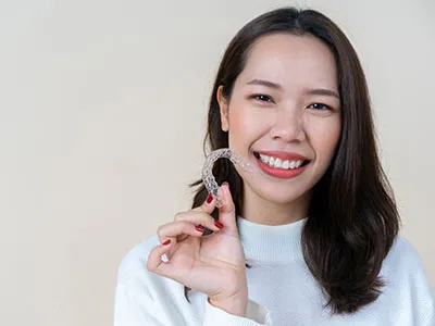 Close up isolated young beautiful Asian woman smiling with hand holding dental aligner retainer
