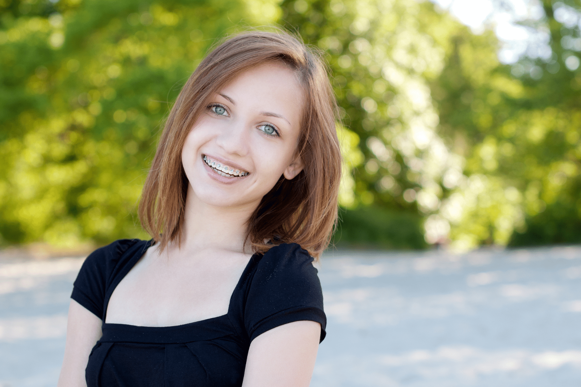 Smiling teenage girl wearing metal braces outdoors.